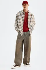 Camisa de manga larga con cuello inglés, tapeta clásica y canesú en la espalda. Presenta un bolsillo superior abierto y bajo redondeado. El tejido es suave de algodón con un patrón de cuadros en tonos celeste, marrón y beige.