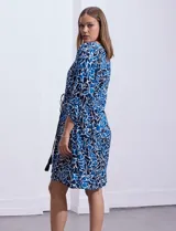 Vestido corto de rayón con estampado floral en tonos azules y blancos. Tiene escote en V, mangas 3/4 con puño, cintura con lazo de ajuste y borlas.