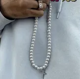 Collar de perlas blancas con dije de cruz plateada con incrustaciones de strass.