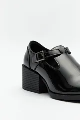 Zapato tipo T-bar de charol negro con hebilla lateral y taco ancho.