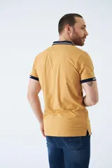 Remera tipo polo color ocre, de corte clásico, con cuello y mangas con terminaciones a contratono en azul marino y blanco.