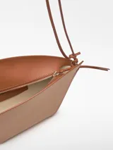 Bolso de hombro de cuero color beige y negro, con forma geométrica asimétrica y asa fina negra.