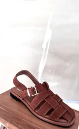 Sandalias bajas color marrón con tiras de cuero entretejidas y hebilla lateral.
