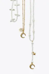 Set de tres collares de diferentes largos. Uno de perlas de diferentes tamaños con cierre de mosquetón. Otro de eslabones metálicos dorados con colgantes en forma de sol y luna. El tercero de perlas de diferentes tamaños con colgantes metálicos dorados en forma de luna labrada y estrella.