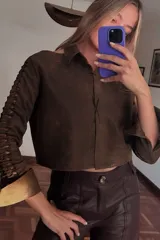 Camisa corta marrón de cuero ovino desgastado con cuello clásico, cierre frontal con botones y mangas largas con aberturas.