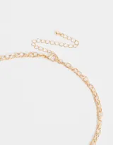 Collar doble dorado, uno con cadena de eslabones y dijes de corazones, y otro con perlas y dije de cruz con detalles de perlas.