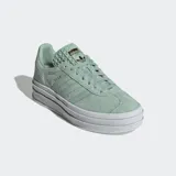 Championes Adidas Gazelle Bold color verde agua con plataforma blanca de triple capa. Presentan las tres tiras clásicas de Adidas en los laterales y la inscripción "Gazelle" en dorado. Confeccionados en gamuza y suela de goma.
