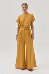 Pantalón de lino color mostaza, de corte palazzo, con lazo en la cintura, pinzas en el frente y bolsillos laterales.