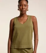 Musculosa de piquet color verde oliva, con escote en pico, breteles anchos, pequeñas aberturas laterales y bajos con pespuntes.