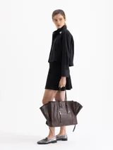 Bolso tote negro de cuero vacuno con textura granulada. Presenta cierres funcionales en los laterales para expandir el espacio y dos asas de mano. Incluye un tag colgante con aplique metálico y un tirador de cremallera con forma de figura.