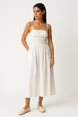 Vestido midi de algodón color blanco, con breteles finos y cuello recto. Presenta un diseño con cintura elástica fruncida y falda de corte evasé.
