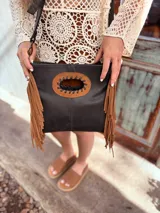 Cartera bandolera negra de cuero con forro interno de tela, detalle de flecos de cuero marrón en la parte inferior y asa larga regulable.