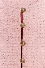 Chaqueta de punto color crema con cuello redondo, manga corta con volantes, bolsillos de plastrón y cierre frontal con botones metálicos.