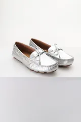 Mocasines plateados de cuero con cordones decorativos y suela de goma marrón.