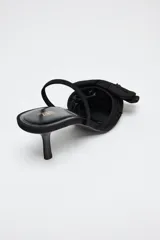 Zapato destalonado negro con tacón fino, capellada de mesh bordado y lazo decorativo en la parte delantera.