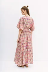 Vestido largo cruzado con estampado floral en tonos rosa, lila y dorado. Tiene mangas cortas amplias, escote en V y cintura elastizada con lazo.