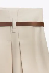 Falda midi color crema de tiro alto con cinturón marrón con hebilla metálica.