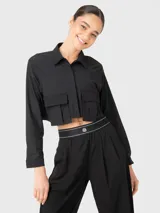 Blusa negra corta de manga larga con cuello camisero, cierre frontal con botones y dos bolsillos con fuelle en el pecho.