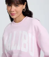 Buzo de algodón y poliéster color rosa claro, con cuello redondo y manga larga. Presenta un estampado grande en el frente con el texto "MALIBU CALIFORNIA BEACH" en letras blancas.