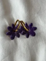 Par de aros colgantes con forma de flor color violeta con glitter y aro dorado.