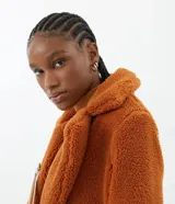 Campera larga de sherpa color marrón, con cuello solapa, cierre con botones y bolsillos laterales. Forro de poliéster.