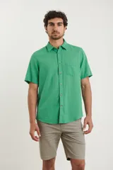 Camisa sport de manga corta color verde oliva, línea premium, con cuello clásico, cierre frontal con botones de coco y bolsillo de parche en el pecho. Confeccionada en lino y algodón.