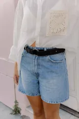 Cinturón de cuero negro liso con hebilla metálica redonda de color plateado.