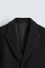 Abrigo negro regular fit confeccionado en paño con lana. Tiene cuello con solapas de muesca, manga larga, bolsillos de solapa en la cadera, bolsillo interior, abertura en el centro de la espalda y cierre frontal con botonadura.