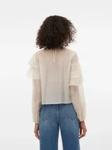 Blusa color crema con volados, cuello redondo y mangas largas con puños abotonados.