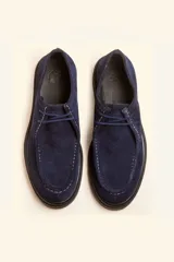 Zapato tipo wallabee de gamuza azul con costuras blancas a la vista y suela de goma negra con plataforma.
