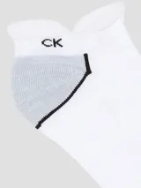 Pack de tres pares de medias invisibles (tipo soquete o tobilleras) de Calvin Klein. Son predominantemente blancas con puntera y talón en gris jaspeado. Presentan el logo "CK" en la parte superior y la inscripción "Calvin Klein" en la planta del pie.