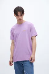 Remera de manga corta color lila con cuello redondo y parche con texto en el pecho.