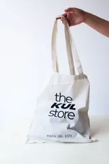 Bolso tipo tote bag de tela color crudo con asas largas y estampado negro con el texto "the KUL store PUNTA DEL ESTE".