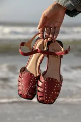 Sandalias cangrejeras color rojo con detalles de tachas doradas y correa con hebilla al tobillo.