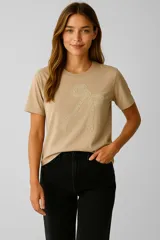 Remera color beige con aplique de moño bordado en el frente, cuello redondo y mangas cortas.