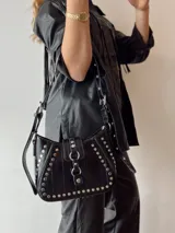 Cartera bandolera negra con tachas plateadas y correa regulable.