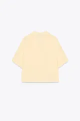 Camisa color amarillo pálido de tejido fluido, con cuello solapa, escote pico, manga corta, bolsillo de parche en el pecho y cierre frontal con botones.