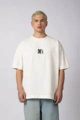 Remera color crema de corte oversize con la inscripción '90's' bordada en el frente y parche con imagen en la espalda.