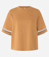 Blusa boxy de mangas cortas amplias, confeccionada en algodón, con cuello redondo y detalle de entremedios en las mangas.