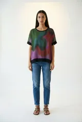 Remera poncho con estampado abstracto en tonos verdes, azules, rojos y violetas, con cuello y mangas con terminaciones en color negro.