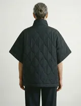 Poncho acolchado color mostaza con cuello alto y abertura frontal con cierre. Presenta un patrón capitoné de formas ovaladas y bolsillos delanteros.