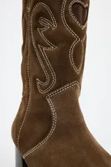 Bota alta de cuero color marrón con bordados en color blanco y negro.