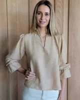 Blusa color beige con cuello con volados, mangas largas abullonadas con puños elásticos y cierre con botones en la parte delantera.