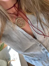 Collar con colgante dorado en forma de espiral y cordón rojo.