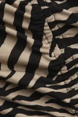 Vestido tobillero ajustado sin mangas, con escote redondo y estampado de cebra en tonos beige y negro. Presenta costura fruncida en el frente para crear un efecto drapeado.