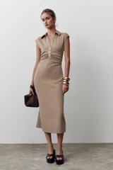Vestido midi color beige con cuello polo, escote en pico, manga sisa caída y detalle de drapeado lateral. Cierre frontal con botones metálicos en relieve.