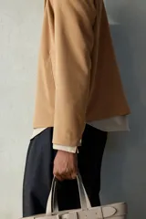 Campera color marrón claro de tejido suave con cuello clásico, cierre frontal con cremallera, bolsillos laterales insertados al bies y puños ajustables con botón a presión.