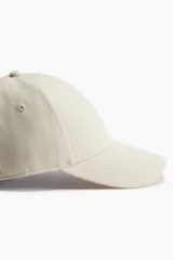 Gorra deportiva color beige, de tejido funcional repelente al agua, con cinta antitranspirante y trabilla ajustable con cierre de metal en la parte posterior.
