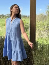 Vestido verde militar de lino, corte a la rodilla, sin mangas, con cuello mao y botones de nácar. Presenta varios cortes en su largo, aportando movimiento y un toque moderno a este diseño fresco y elegante.