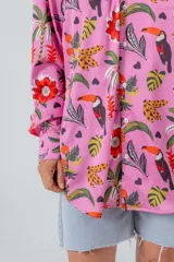 Camisa de seda blanca con estampado de flores rojas, palmeras, piñas y tucanes. Tiene cuello clásico, mangas largas y corte recto.